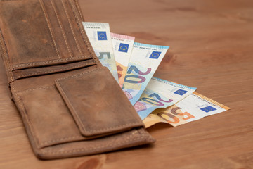 Opened leather wallet with euro banknotes on a wooden table 