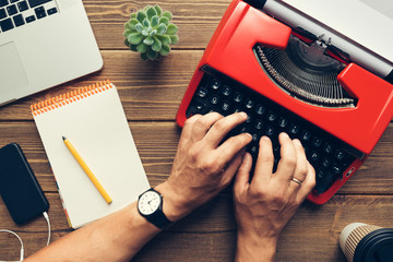 Top view close up of mans hands using vintage red typewriter placed on wooden desk