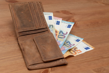 Opened leather wallet with euro banknotes on a wooden table 