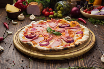 Delicious italian pizza with ham, sausages and onion decorated by basil leaves on wooden background