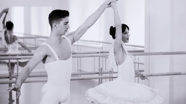 Young man practicing in classical ballet with beautiful woman in tutu dress in gym or ballet hall. Couple perform a sensual dance. Minimalism interior. Black and white tonned,