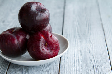 three red plums on a plate on a grey wooden table