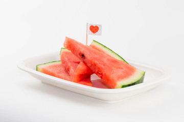 Isolated sliced fresh watermelon on a plate with a cute red heart flag.