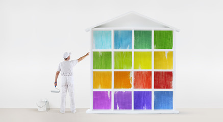 rear view of painter man pointing with finger the colors house model on wall, with paint roller and...