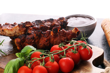 Spicy hot grilled spare ribs from a summer BBQ served with fresh tomatoes on an old vintage wooden cutting board