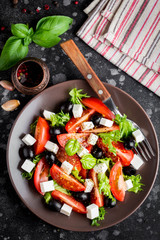 Salad with tomatoes, feta, olives and Basil, serving on a dark background