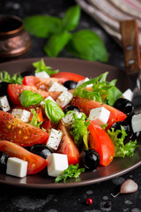 Salad with tomatoes, feta, olives and Basil, serving on a dark background