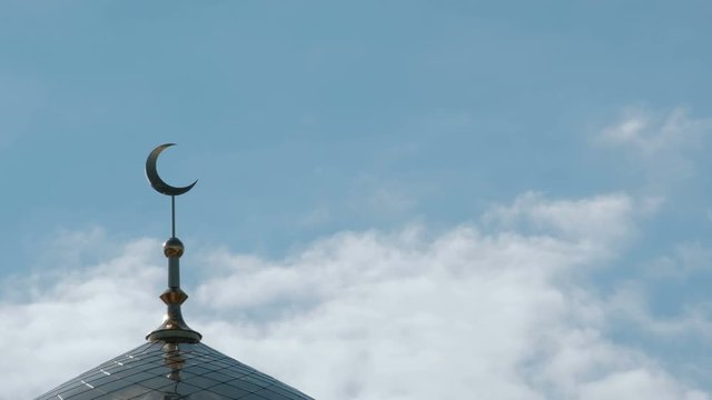 A close-up of a Muslim crescent on a minaret in the sky with clouds.