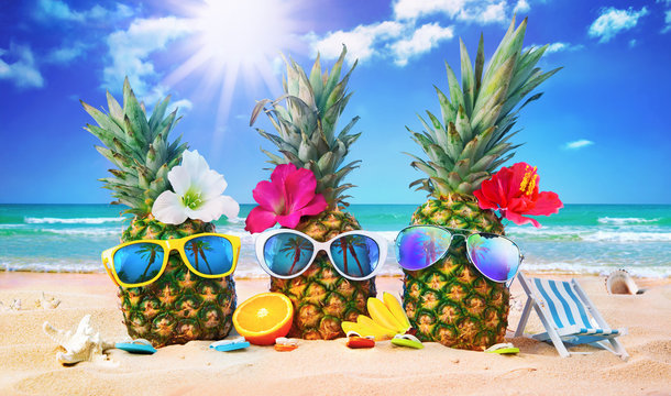 Attractive pineapples in stylish sunglasses on the sand against turquoise sea