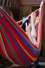 young woman relaxing in colorful hammock and using smartphone