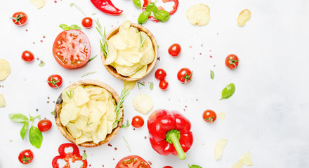 Unhealthy food background, potato chips with salt, tomatoes, chili and bell pepper, spices and green basil, top view