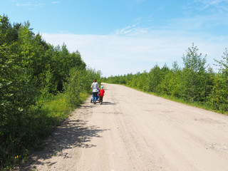 woman with a stroller walks along a dirt road in the forest