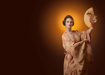 Young beautiful woman in traditional Japanese kimono dancing with a fan.