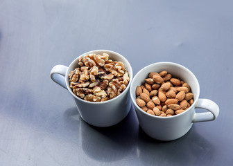 White cup full of almonds and walnuts on grey background. Above view