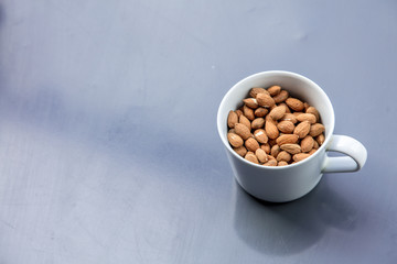 White cup full of almonds on grey background. Above view
