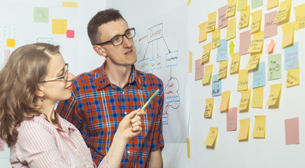 Business people discuss and plan creative work, making notes on paper stickers. A young man and a woman use the post it for new ideas.