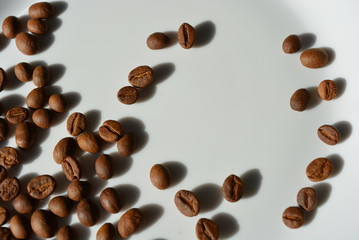 On a white glass plate, the delicious and edible brown coffee beans laid and beautifully arranged