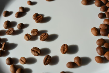 On a white glass plate, the delicious and edible brown coffee beans laid and beautifully arranged