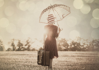 photo of the beautiful young woman with red umbrella and brown suitcase standing in the field