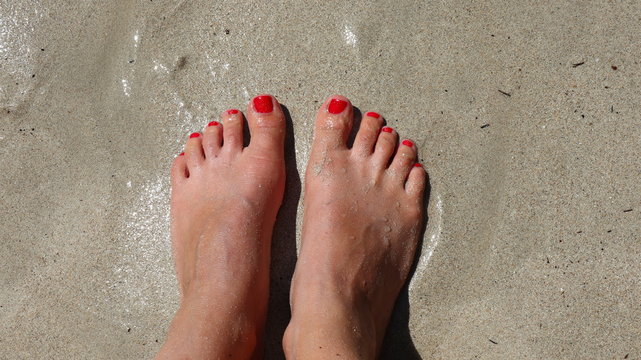 F&uuml;&szlig;e mit rot lackierten N&auml;gel am Sandstrand