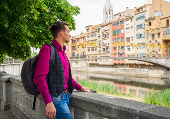 A young guy, tourist, stands with a backpack on the river bank Onyar in Girona, Spain © allai