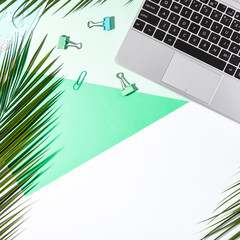 Office table desk, Flat lay, top view. White, green and turquoise backgrond. Palm branches and laptop keyboard