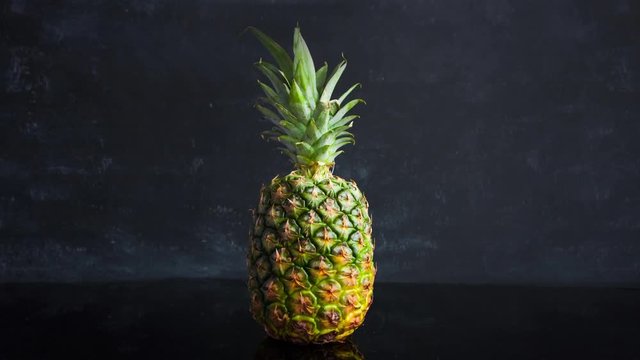 Stop motion ripe tropical fruit pineapple on a black background. Time lapse food footage.