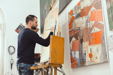 Concentrated male artist is drawing on easel in his art studio, lots of pictures, creative...