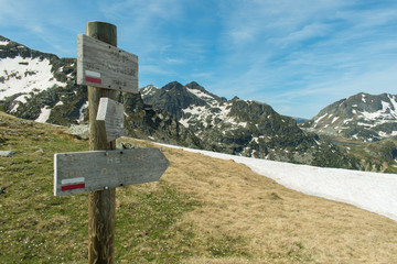 Fingerpost in the French Pyrenees on the GR10 hiking route. The sign is at the Col de Terre Negre and points towards the Refuge du Rulhe, with snowy mountains and a blue cloudy sky background.