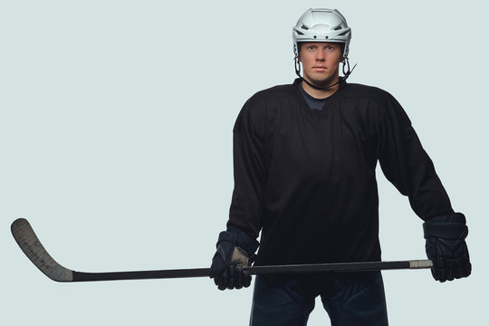 Hockey Player Wearing Black Protective Gear And White Helmet Holds A Hockey Stick On A Gray Background.