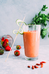 Strawberry smoothie poured  on a glass over on a gray table and a blue background, a cucumber slice as rnament.