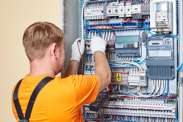 Engineer tests power high voltage three phase circuit box with multimeter.