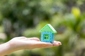 Woman hand hold home block model with blur green background (Concept for dream home, family fulfillment)