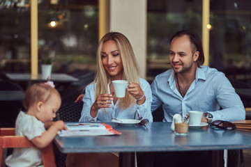 Family and people concept - happy mother, father and the little girl in outdoor cafe.