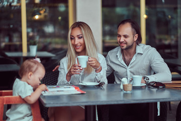 Family and people concept - happy mother, father and the little girl in outdoor cafe.