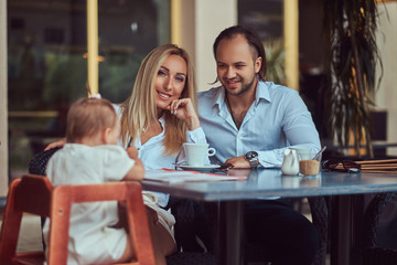 Family and people concept - happy mother, father and the little girl in outdoor cafe.