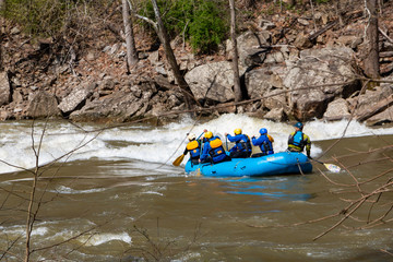 Rafters braving white water rapids in the early spring in a blue inflatable boat.
