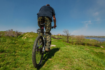 Fototapeta premium Back view of man riding bike on green grass background