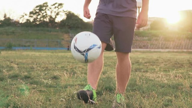 Slow motion football stunts. The football player throws the ball alternately with his feet. A teenager is playing on an abandoned football field at sunset on a sunny day in the summer. Football field