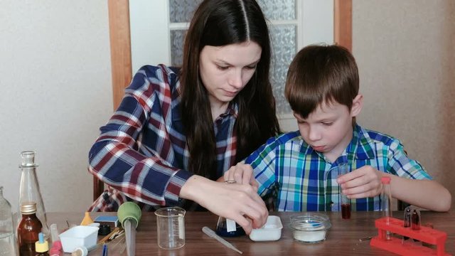 Chemistry experiments at home. Mom and son make a chemical reaction with the release of gas in the test tube.