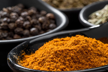 different spices and herbs in spoons or bowls on a brown wooden background . Food and cuisine ingredients  .Dried rosemary,black pepper,red paprika powder or Cayenne Pepper ,oregano close up