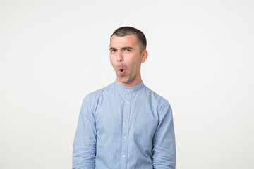 Fototapeta premium Shocked face of caucasian young man in blue shirt on grey background