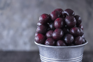 Ripe cherry in a metal bucket on a dark background.