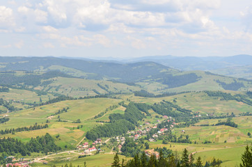 Naklejka na ściany i meble Outstanding landscape from a height. Green forest and village in the mountains against the sky. Ukrainian Carpathians