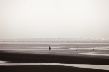 A man walking along black & white sand on the beach 