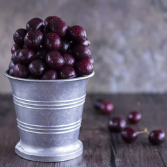 Ripe cherry in metal bucket on  dark wooden background.