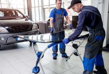Automobile special workers replacing windscreen or windshield of a car in auto service station garage.