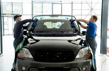 Automobile special workers replacing windscreen or windshield of a car in auto service station...