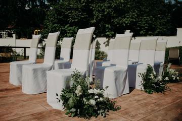 stylish chairs in white covers decorated with fresh flowers for wedding ceremony