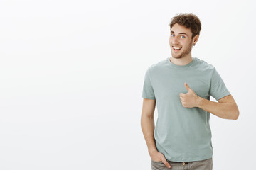 Have not heard ideas better. Portrait of positive good-looking male model with bristle in earrings, turning head in profile and smiling broadly while showing thumbs up, liking plan and giving approval